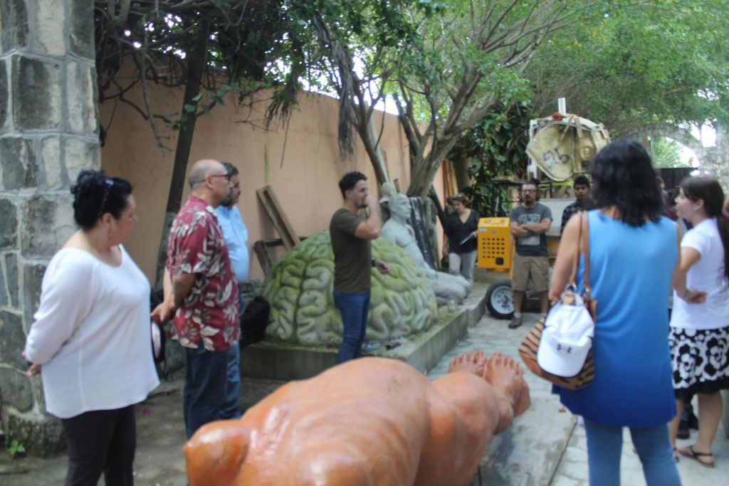한 무리의 사람들이 여러 개의 커다란 조각품과 빽빽한 나무가 있는 야외 공간에서 이야기를 나누고 있습니다.