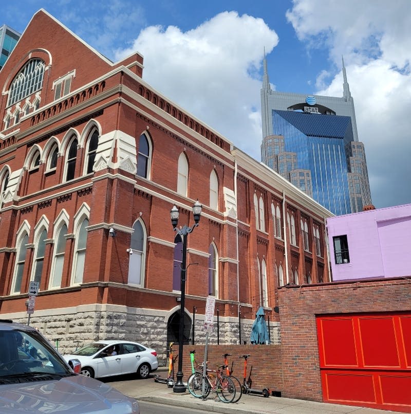 아치형 창문, 배경에 현대적인 고층 건물, 주차된 자동차, 자전거가 있는 유서 깊은 벽돌 건물입니다.