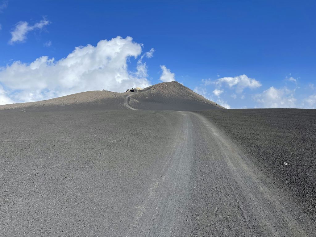 흙길은 구름이 흩날리는 밝고 푸른 하늘 아래 불모의 모래 언덕으로 이어집니다.