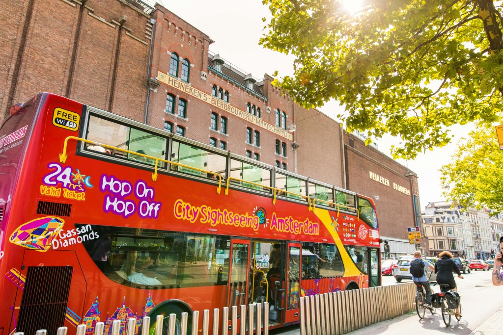 빨간색 이층 도시 관광 버스가 외관에 "하이네켄 Brouwerij" 가 있는 대형 벽돌 건물 근처에 주차되어 있습니다.