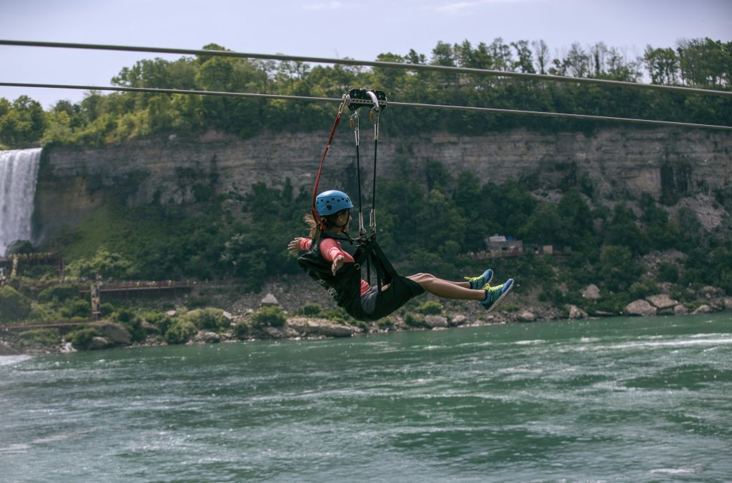 숲이 우거진 절벽을 배경으로 헬멧을 쓰고 강가에서 지퍼 라이닝을 즐기는 사람.