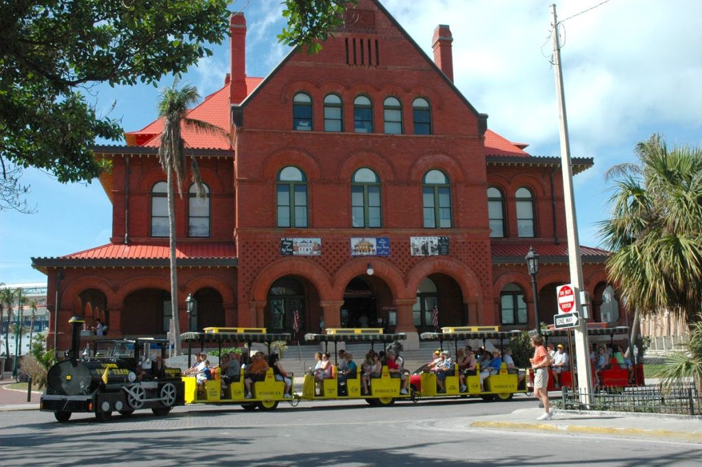 아치형 창문이 있는 유서 깊은 붉은 벽돌 건물 앞에 승객이 주차된 노란색 관광 트롤리가 있습니다.