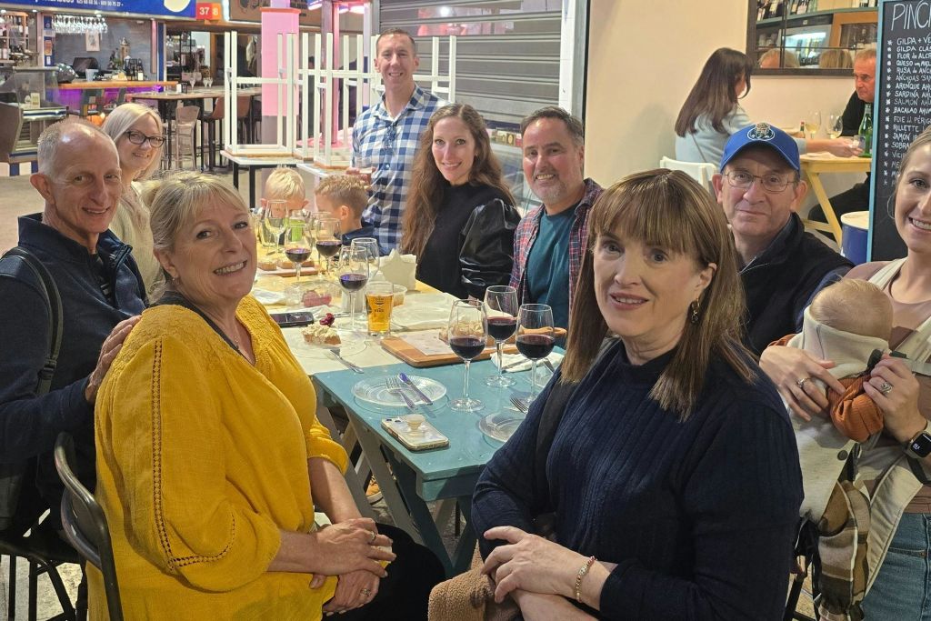 캐주얼한 실내 환경에서 어른 6명과 어린이 2명이 한 테이블에 모여 음료와 음식을 즐기고 있습니다.