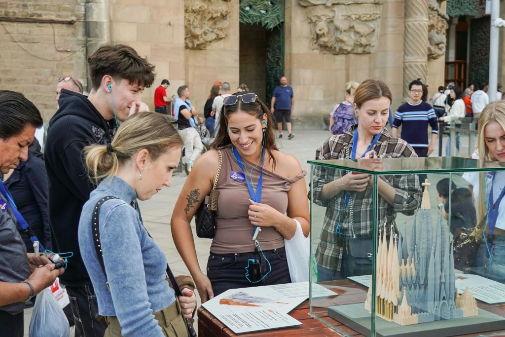 화려한 건물 입구 근처 야외 유리 케이스에 전시된 성당의 규모 모델을 관찰하는 사람들의 모임.