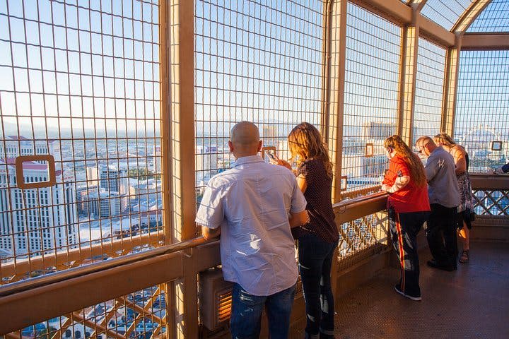해가 질 무렵 도시 풍경이 내려다보이는 철조망 뒤 전망대에 서 있는 사람들.