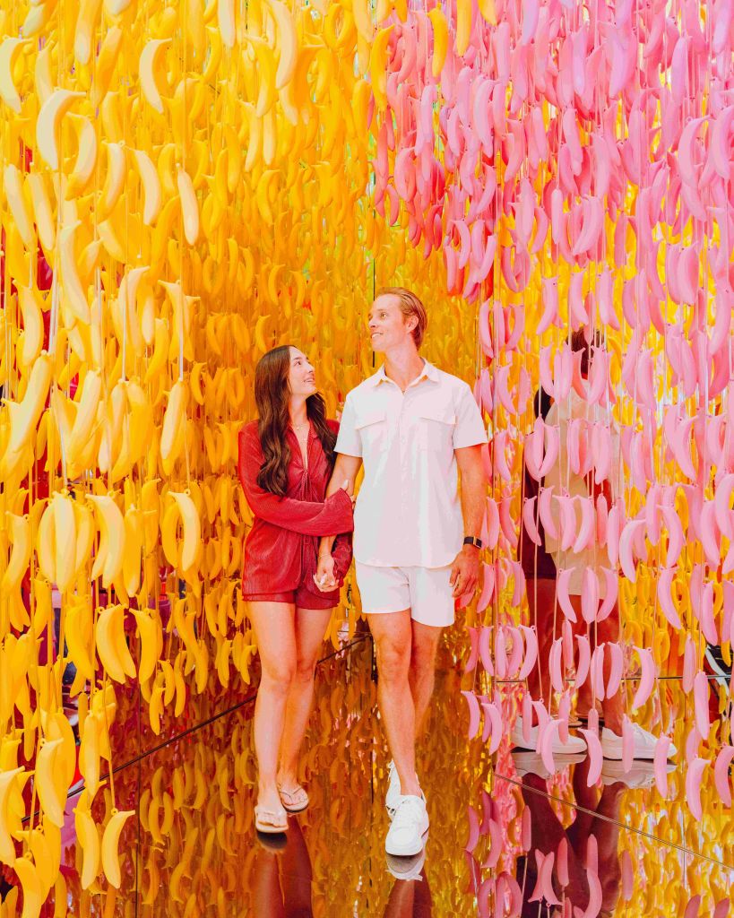 손을 잡고 노란색과 분홍색 바나나 장식이 걸려 있는 다채로운 전시관을 둘러보세요.