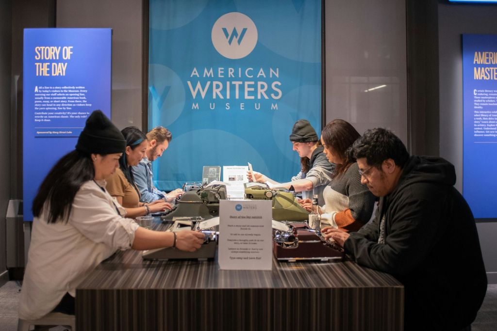 미국 작가 박물관 (American Writers Museum) 의 전시 카운터에서 네 명이 빈티지 타자기를 입력합니다.