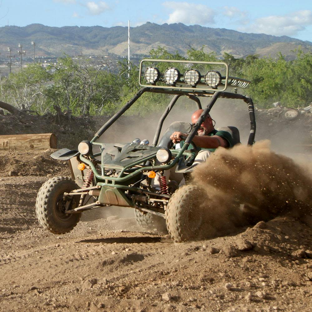 산과 녹지를 배경으로 먼지 구름을 걷어 올리며 모래 언덕을 달리는 사람.