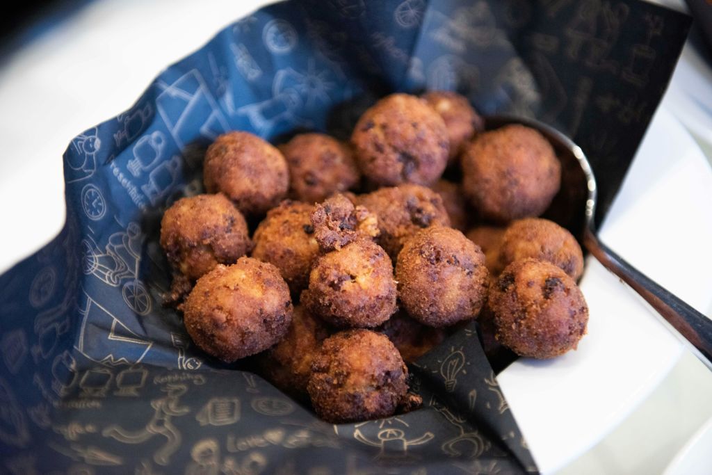 흰색 그릇에 어두운 무늬의 냅킨 위에 놓인 튀긴 황금 갈색 아란치니 볼 더미.