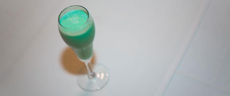 흰색 표면에 청록색 음료를 가득 채운 키 큰 플루트 유리.