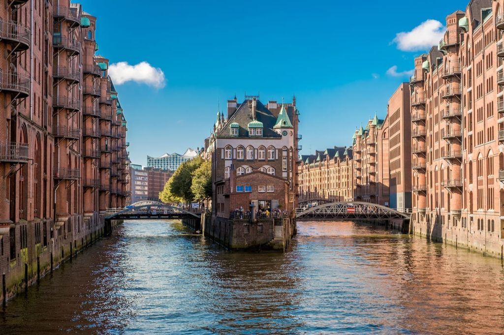 푸른 지붕이 있는 유서 깊은 건물이 벽돌 건물과 다리를 사이에 두고 맑고 푸른 하늘 아래 운하를 가로지르고 있습니다.