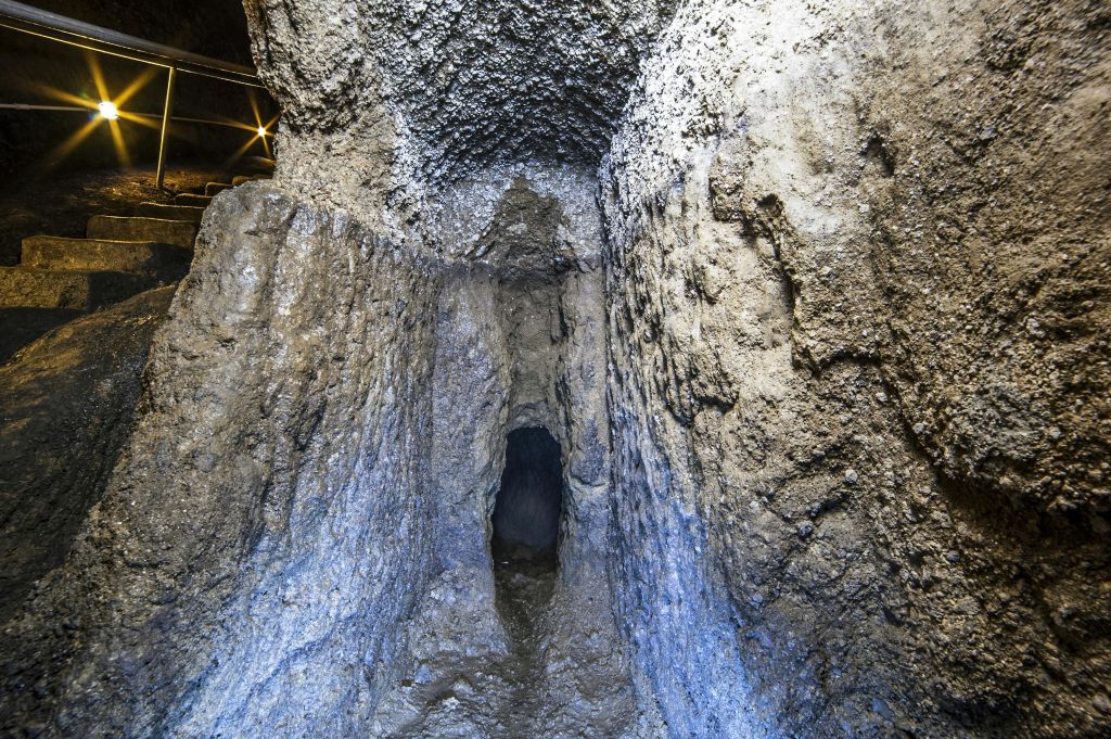 거칠고 질감이 있는 벽이 있는 좁은 돌 터널. 어두운 조명이 동굴 같은 내부를 비춥니다.