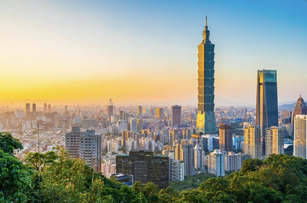 수많은 건물과 녹지로 둘러싸인 높고 독특한 디자인의 고층 건물이 있는 석양의 도시 풍경.