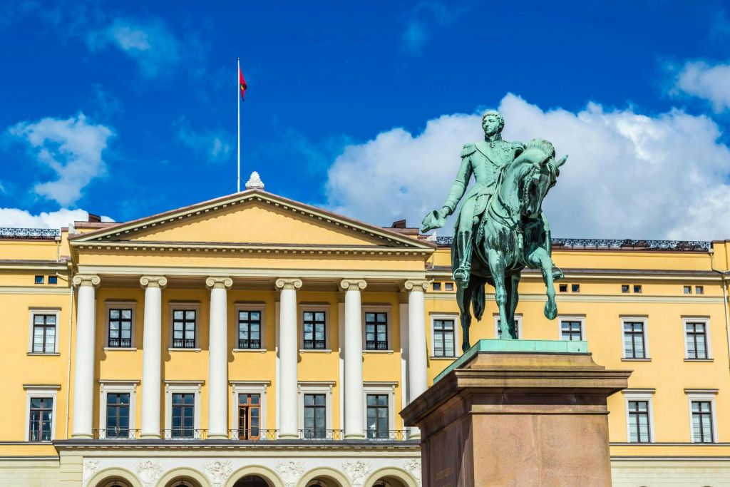 노란색 건물 앞에 기둥이 있는 말을 탄 남자의 동상. 푸른 하늘 아래 건물 꼭대기에서 깃발이 휘날리고 있습니다.