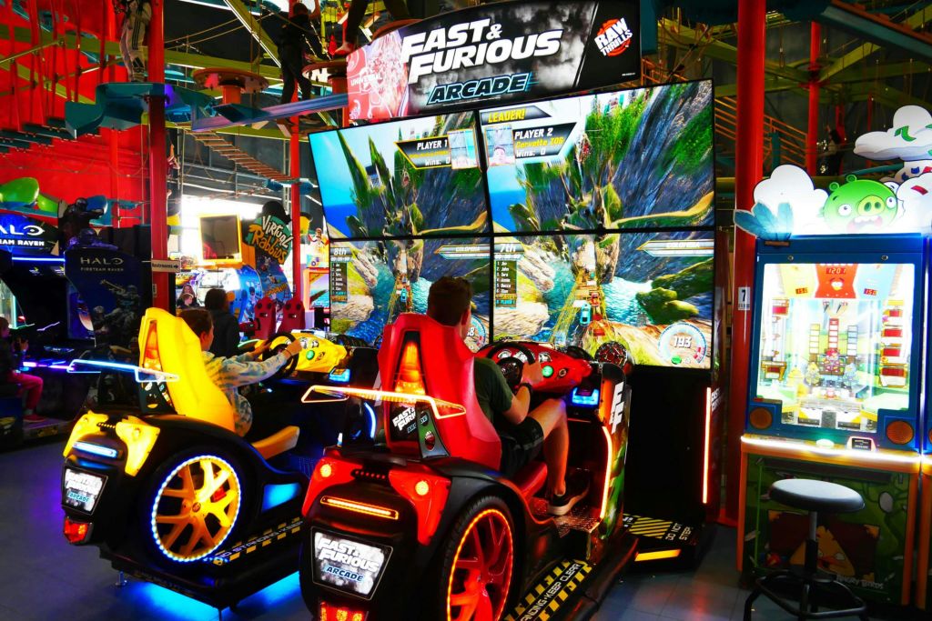 두 사람이 활기찬 화면과 자동차 모양의 좌석이 있는 아케이드 환경에서 Fast & Furious 아케이드 레이싱 게임을 하고 있습니다.