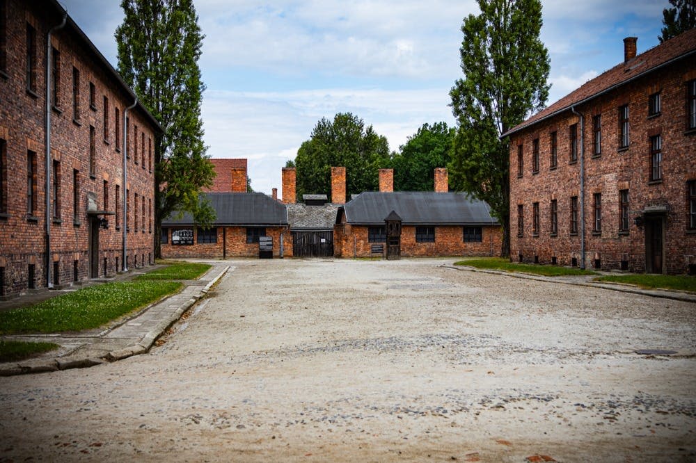 탁한 하늘 아래 높은 굴뚝과 초록을 배경으로 넓고 텅 빈 마당이 붉은 벽돌 건물 옆으로 펼쳐져 있습니다.