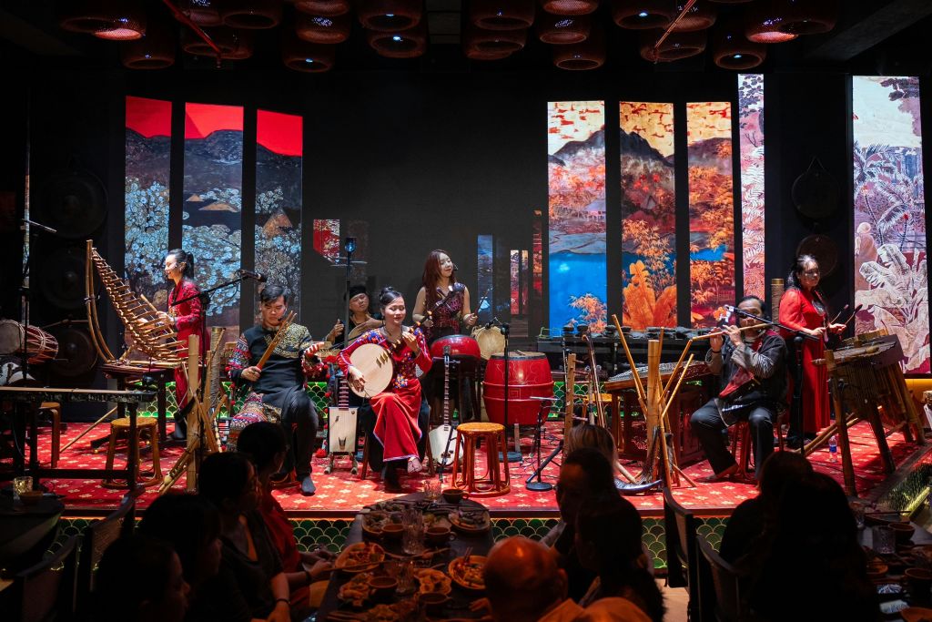아시아 전통 음악 앙상블이 무대에서 활기찬 경치를 배경으로 공연합니다. 음악가들은 다양한 악기를 연주합니다.