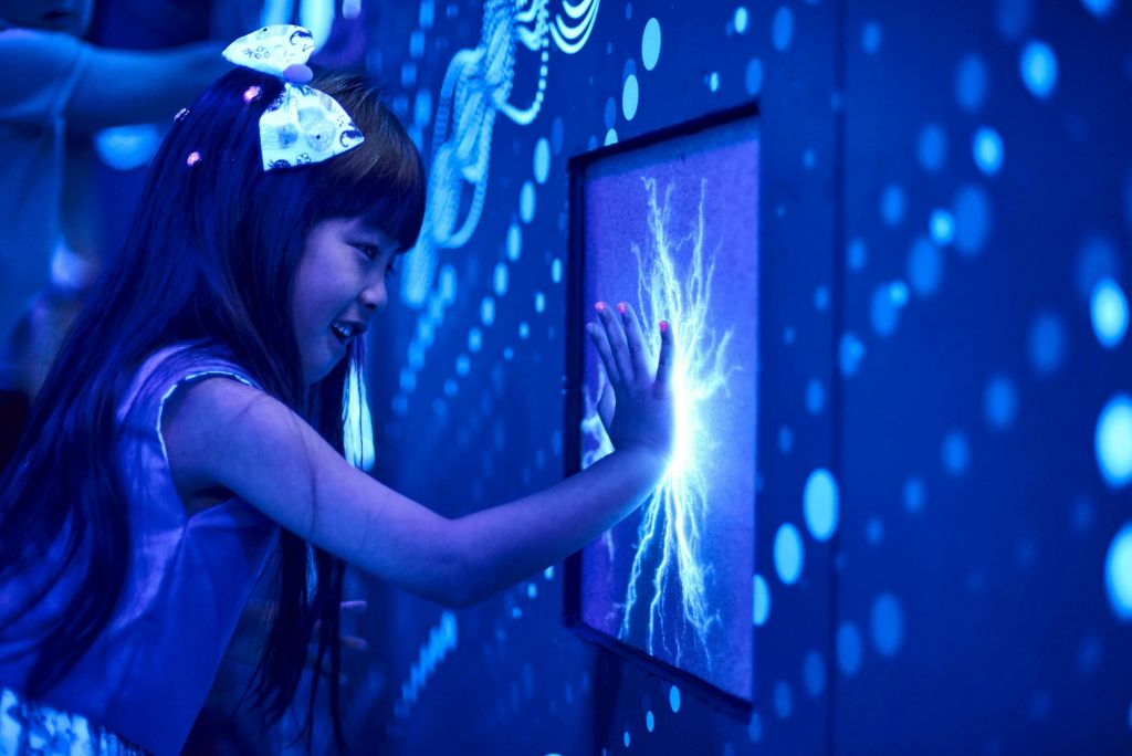 한 소녀가 파란색 조명 환경에서 조명 패턴이 있는 빛나는 대화형 디스플레이를 만지고 있습니다.