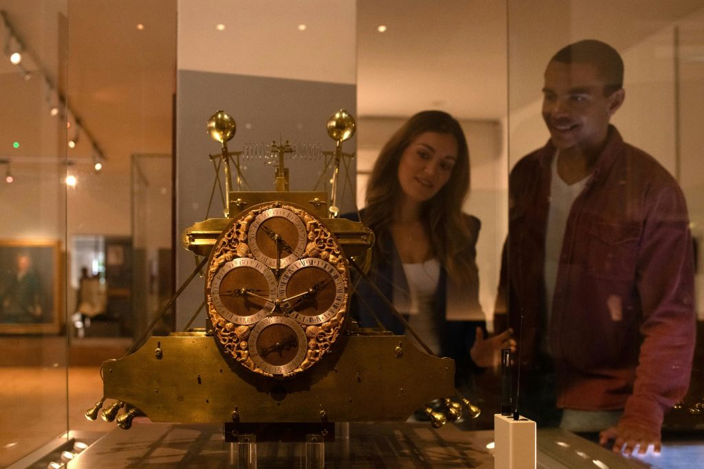 박물관 진열대에 놓인 정교한 골동품 시계를 보며 두 사람이 미소를 짓고 있습니다.