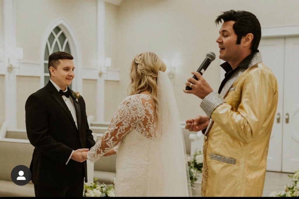 결혼식 중 금색 재킷을 입은 공무원이 마이크를 가리키며 손을 잡고 있는 부부.