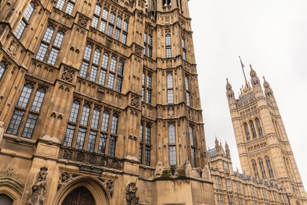 높고 화려한 창문과 섬세한 석조 작품이 있는 고딕 양식의 건축물. 표지판에는 "성 스테파노의 입구" 라고 쓰여 있습니다. 저 멀리 또 하나의 탑이 있다.