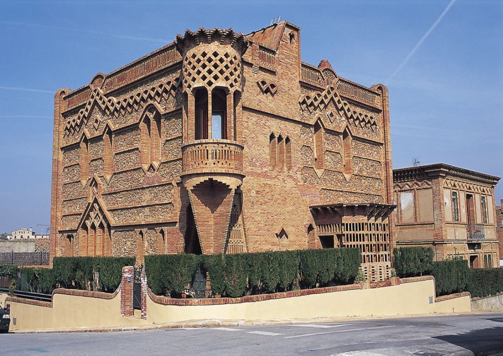 맑고 푸른 하늘 아래, 가장자리를 따라 정교한 기하학적 패턴, 작은 발코니, 녹지가 있는 독특한 벽돌 건물입니다.