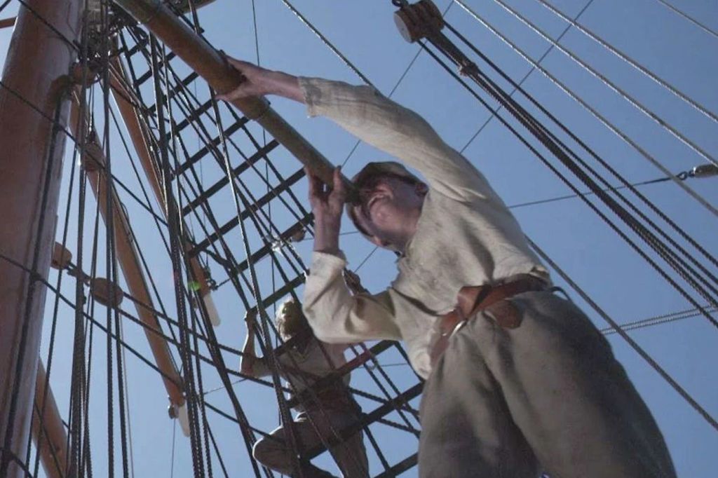 두 사람이 키 큰 배의 리깅에 올라가는데, 하나는 스파이글래스를 뚫어지게 들여다보고 있습니다. 하늘이 맑고 푸르다.