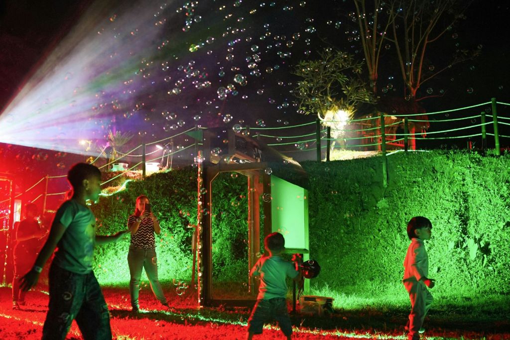 밤에는 야외에서 거품을 내며 놀고, 주변과 녹지를 비추는 다채로운 조명과 함께 놀고 있는 어린이들.