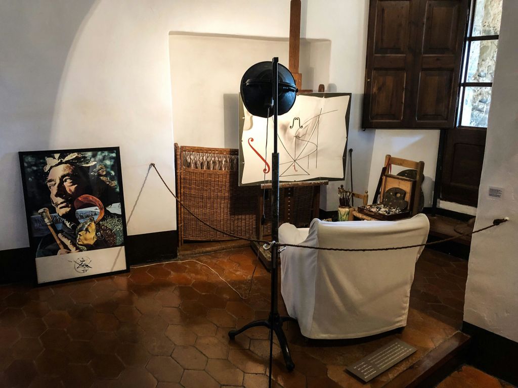 흰색 의자가 있는 아트 스튜디오, 추상적인 그림이 있는 이젤, 머리 위 조명, 바닥에 액자 그림, 목재 가구.