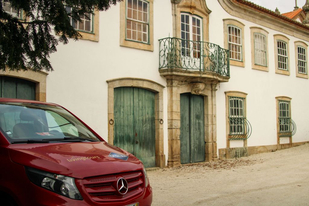 녹색 문과 연철 발코니가 있는 흰색 건물 앞에 빨간색 메르세데스 밴이 주차되어 있습니다.