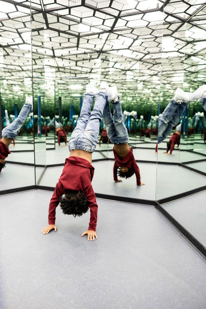 미러룸에서 여러 각도의 자세를 비추며 핸드스탠드를 하는 아이.