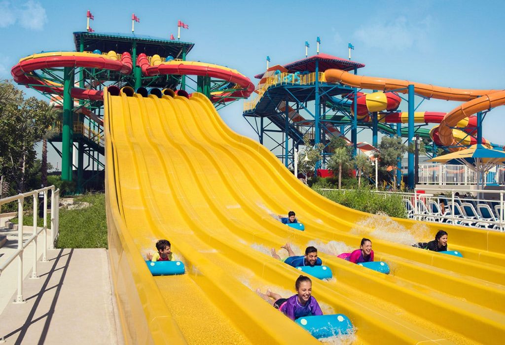 다채로운 색상의 워터파크에서 파란색 매트를 착용한 사람들이 노란색 워터 슬라이드를 따라 내려오고 있습니다.