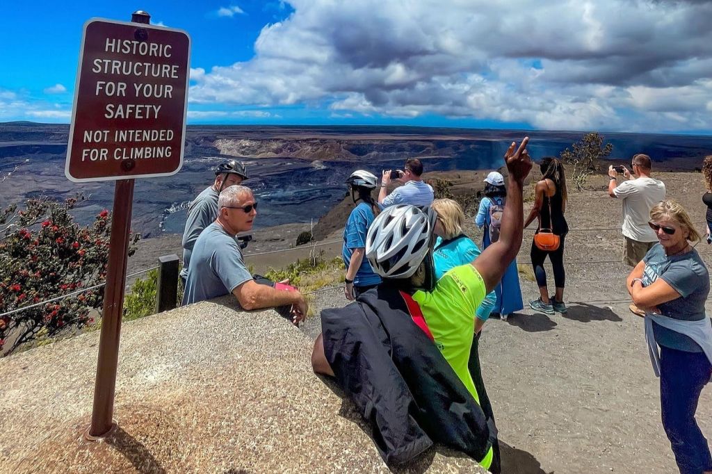 경치 좋은 전망을 자랑하는 관광객들은 전경에 "Historic Structure For Your Safety" 표지판이 있는 화산 지형을 조망할 수 있습니다.