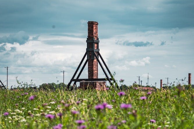 흐린 하늘 아래 야생화 밭에 구조적 지지대가 있는 높은 벽돌 연막이 서 있습니다.
