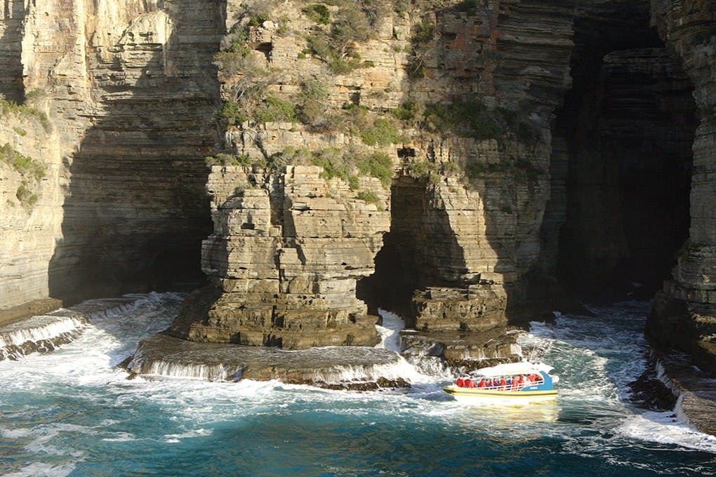 노란색과 빨간색 캐노피가 있는 작은 보트가 바위에 물이 부딪히는 바위 절벽 근처에 있습니다.