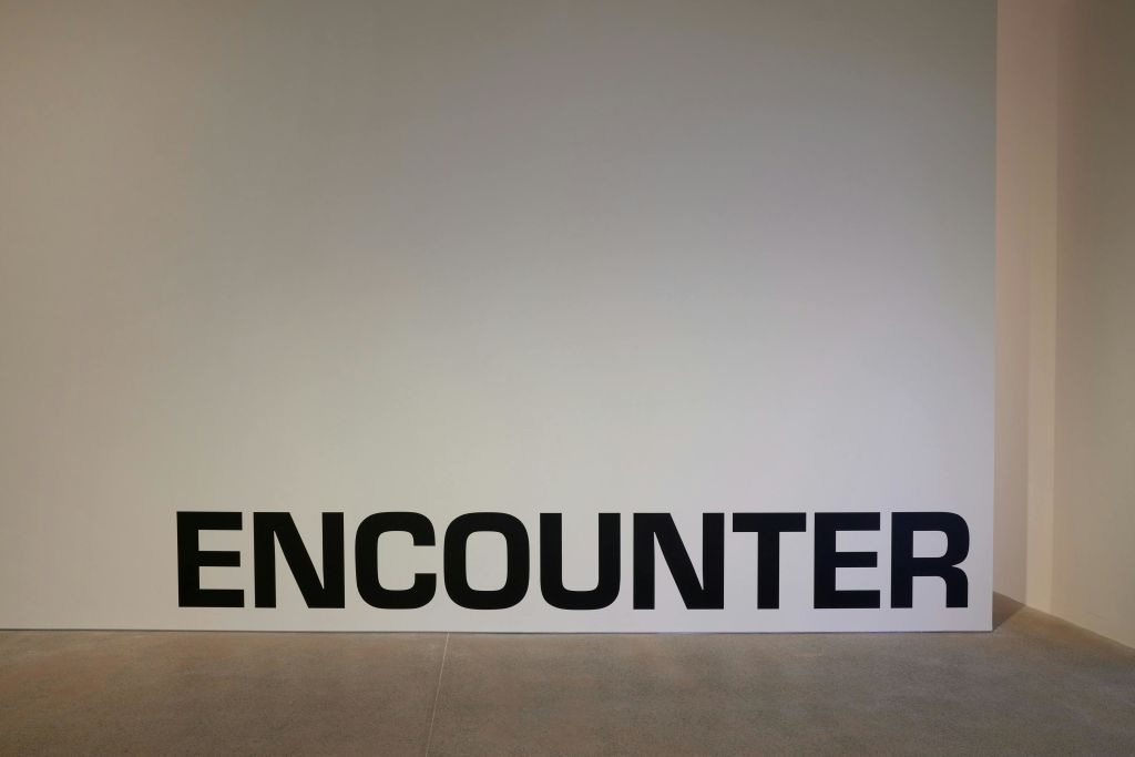 하단 근처에 크고 굵은 검은 글씨로 '만남' 이라는 단어가 적힌 하얀 벽.