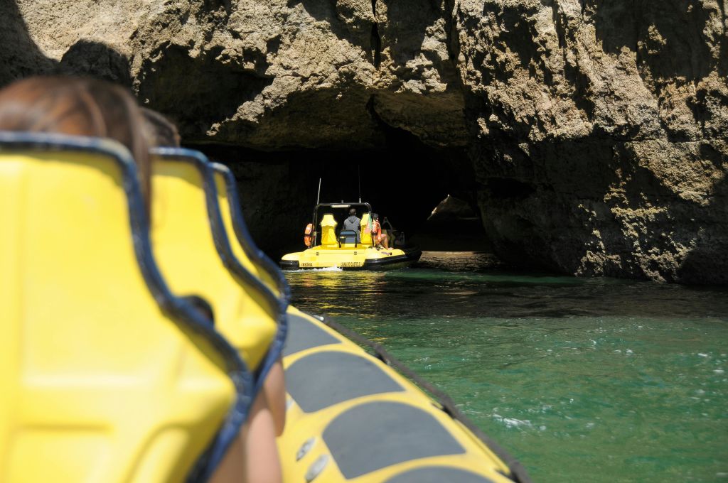 초록색 물 위로 바위 동굴 입구에 접근하는 노란색 팽창식 보트를 탄 사람들.