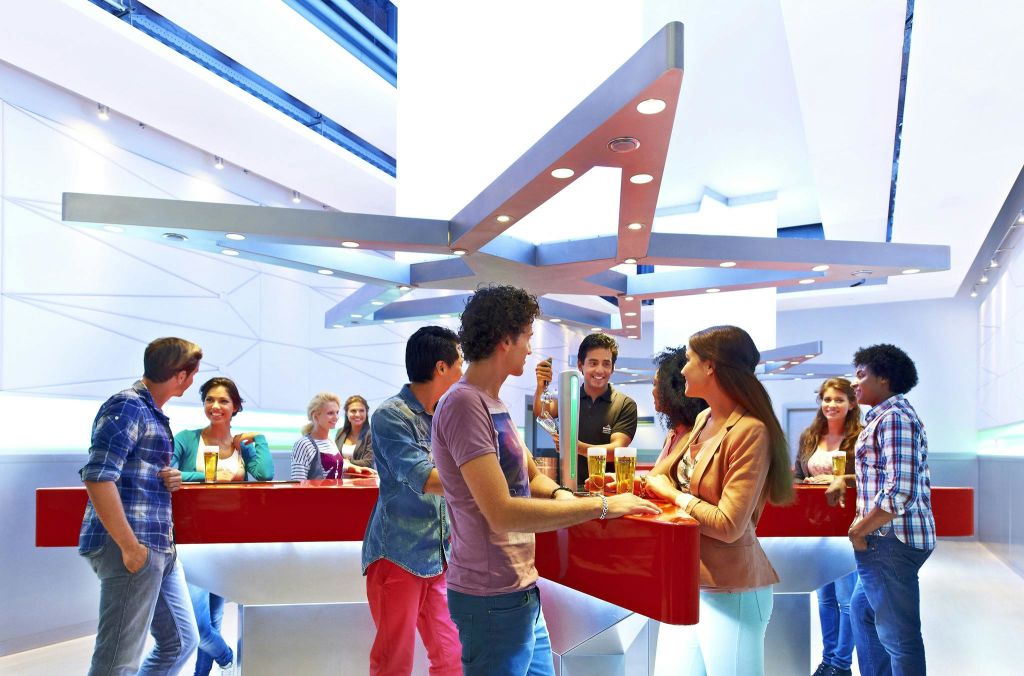 머리 위로 빨간색 카운터와 금속 구조물이 있는 현대적인 바에서 어울리는 사람들, 음료를 들고 대화에 참여하는 사람들.