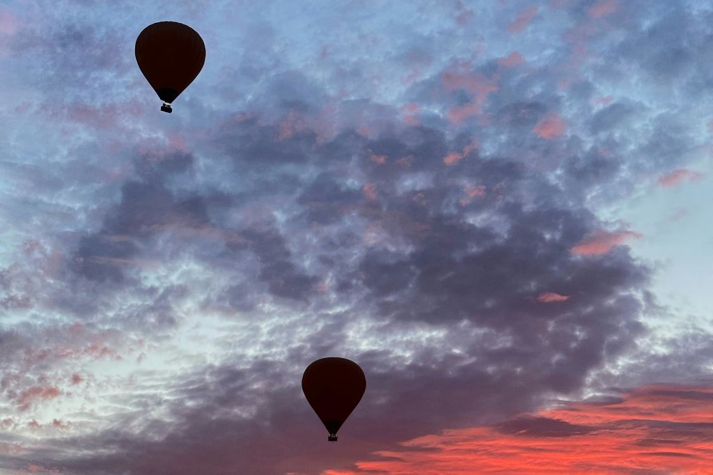 일출이나 일몰에 알록달록한 하늘을 배경으로 분홍색과 보라색으로 물든 두 개의 열기구.
