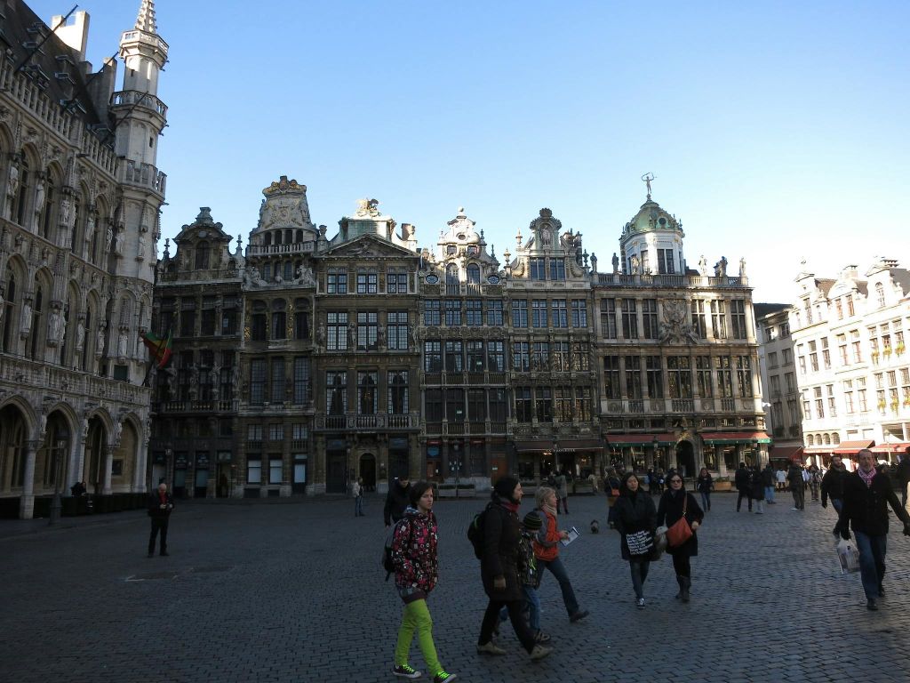 화려한 역사적 건물과 맑고 푸른 하늘을 배경으로 커다란 광장을 걷는 사람들.