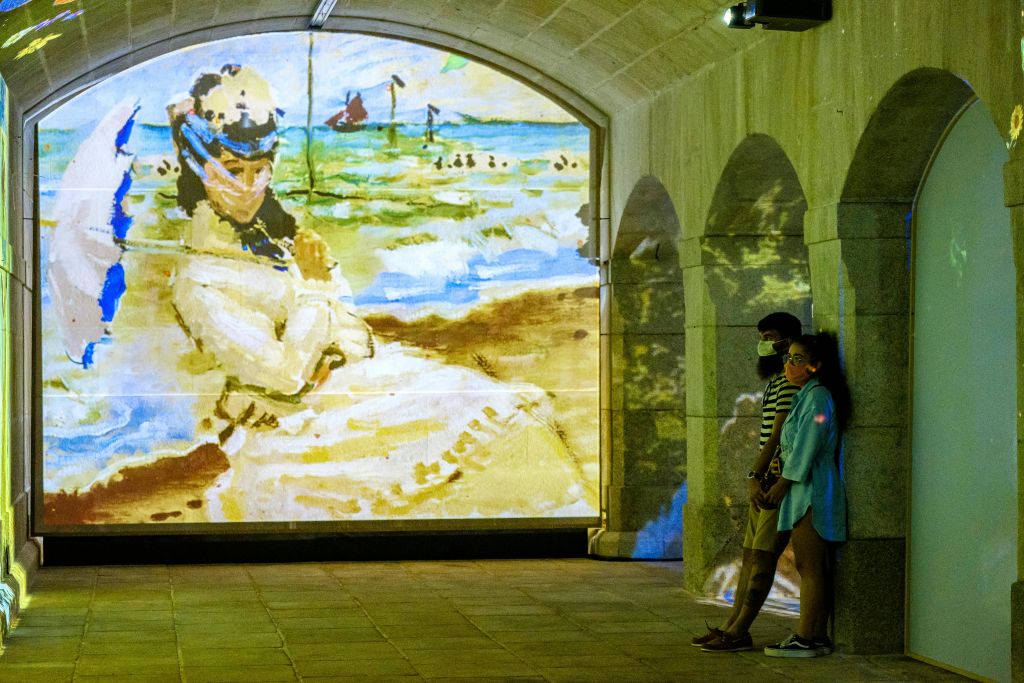 두 사람이 아치형 복도에 서서 여성과 해변 장면이 담긴 그림의 생생한 디지털 투영을 관찰합니다.