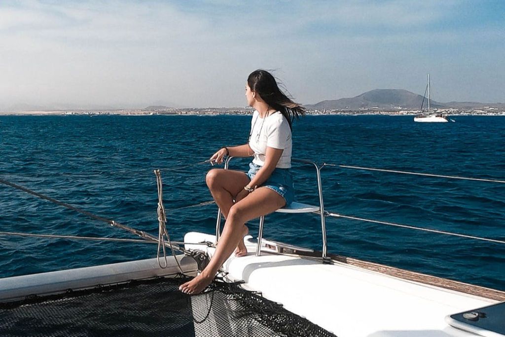 요트에 앉아 산을 배경으로 푸른 바다를 바라보는 사람.