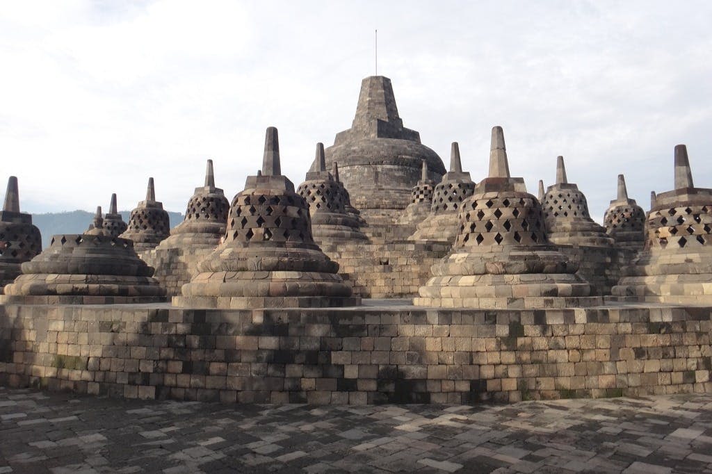 여러 종 모양의 스투파와 흐린 하늘 아래 중앙 돔이 있는 고대 석조 사원 구조물.