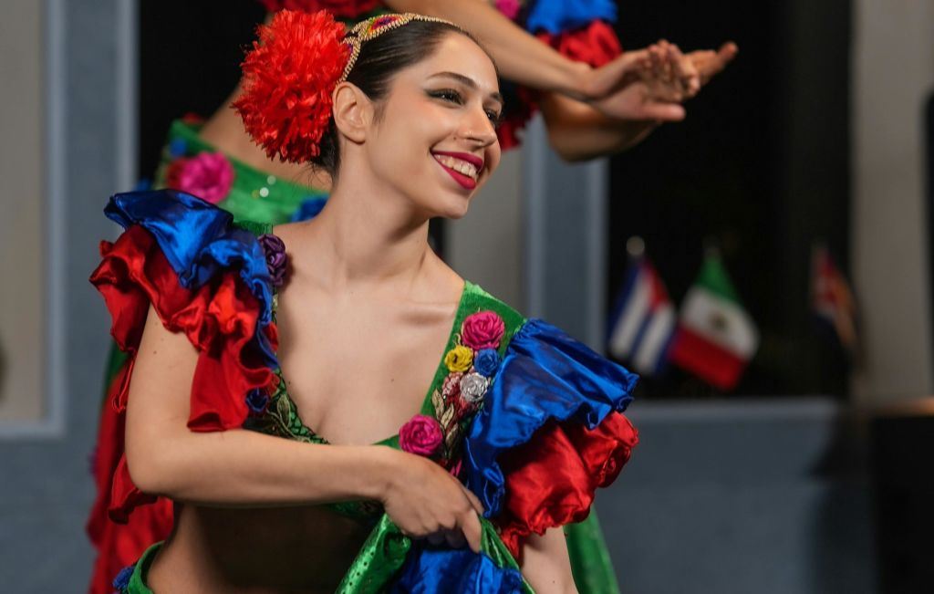 활기찬 빨간색, 파란색, 녹색 원단을 사용한 화려한 전통 복장을 한 여성이 춤을 추며 미소를 짓고 있습니다.