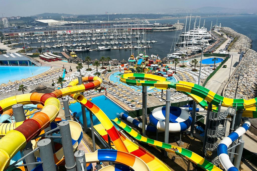 요트와 보트로 가득한 정박지 옆에 다채로운 미끄럼틀과 수영장이 있는 워터파크.