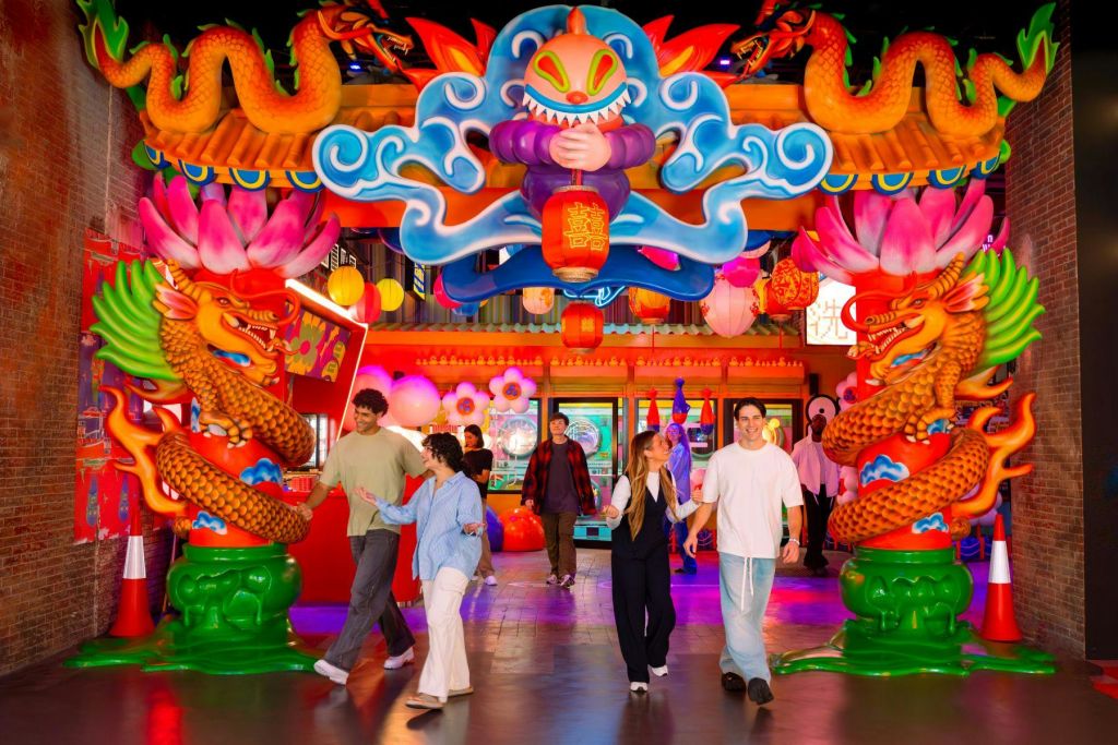 드래곤 동상과 사람들이 걷고 디스플레이와 상호 작용하는 등 밝은 장식을 갖춘 다채로운 실내 장면.