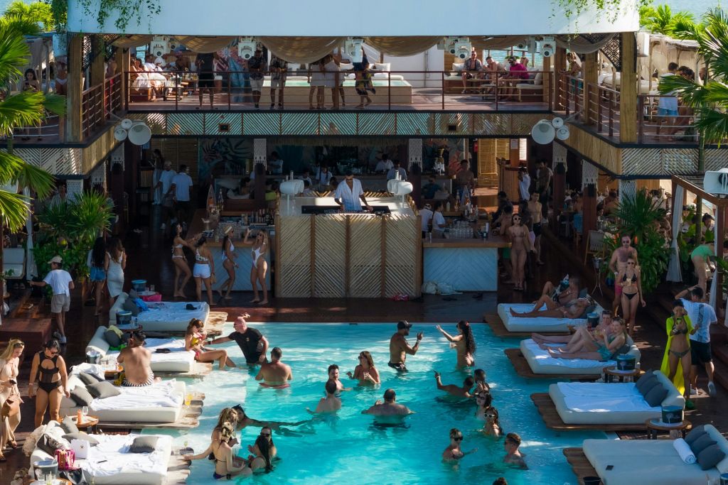 상부 및 하부 데크 공간이 있는 흰색 데이베드에서 음악, 춤, 휴식과 함께 수영장 파티를 즐기는 사람들.