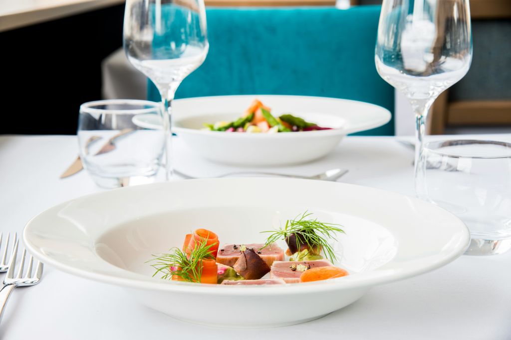 고급 음식 두 접시, 와인잔, 청록색 의자를 배경으로 우아한 테이블 분위기가 연출됩니다.