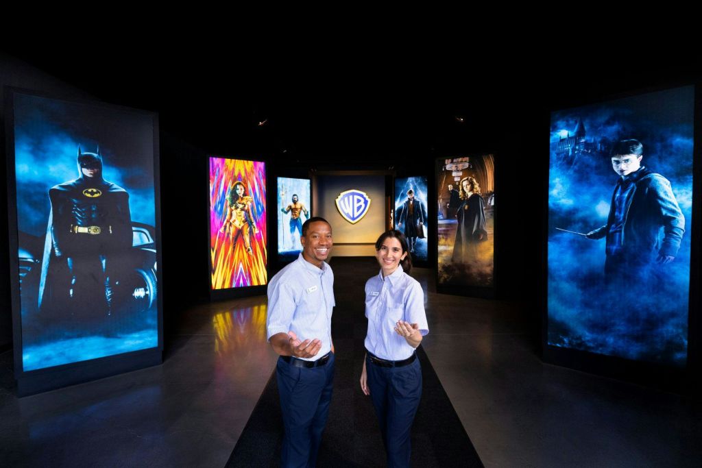 영화 캐릭터의 대형 포스터와 배경에 워너 브라더스 로고가 있는 전시장에 유니폼을 입은 두 사람이 서 있습니다.
