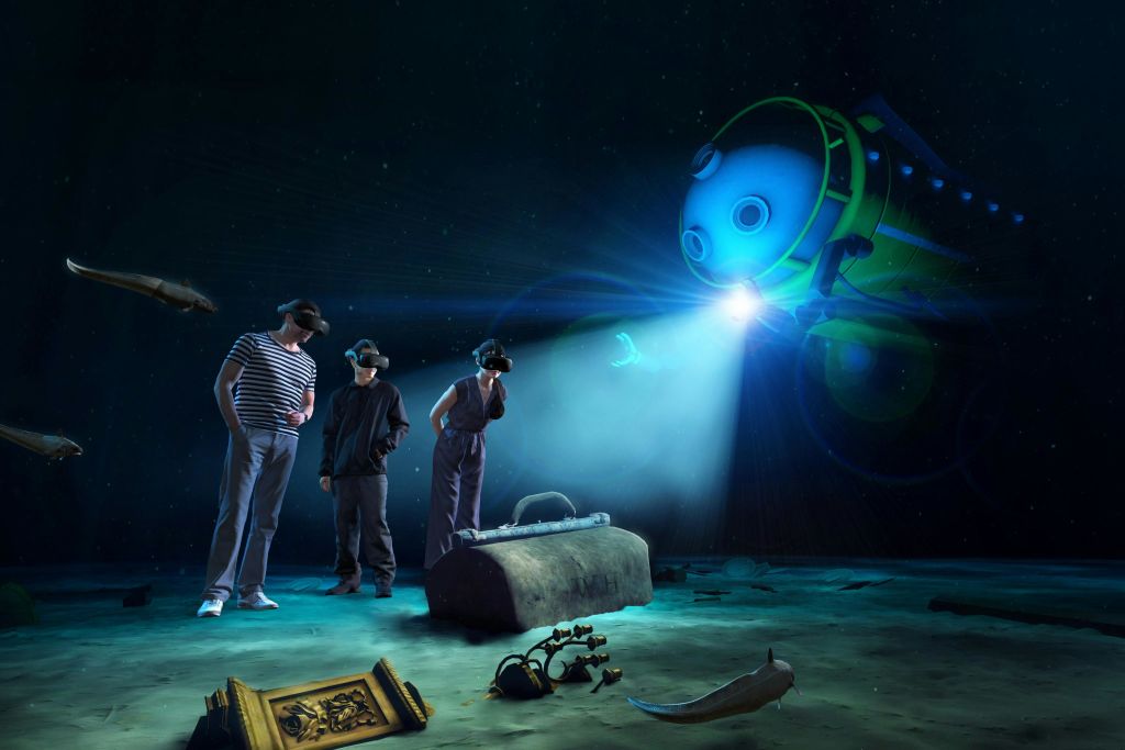 VR 헤드셋을 착용한 세 사람이 난파선, 보물 상자, 잠수정을 들고 시뮬레이션된 수중 장면에 서 있습니다.